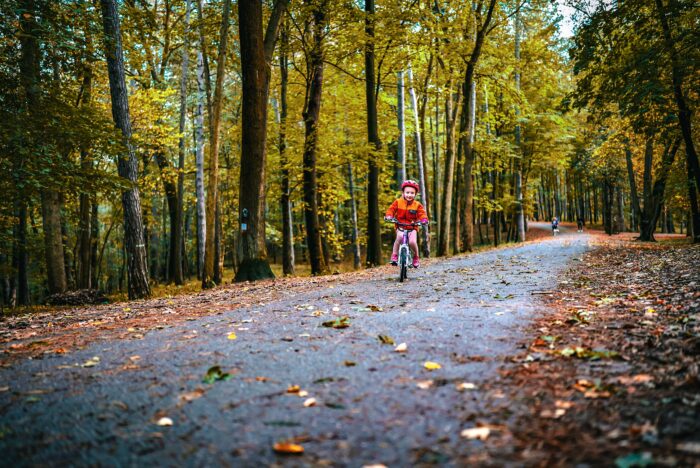 dievča na bicykli vezúce sa cestou v strede jesenného lesa